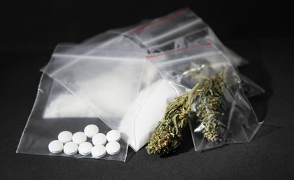 a pile of small plastic bags containing white powder, white pills and dry green leaves